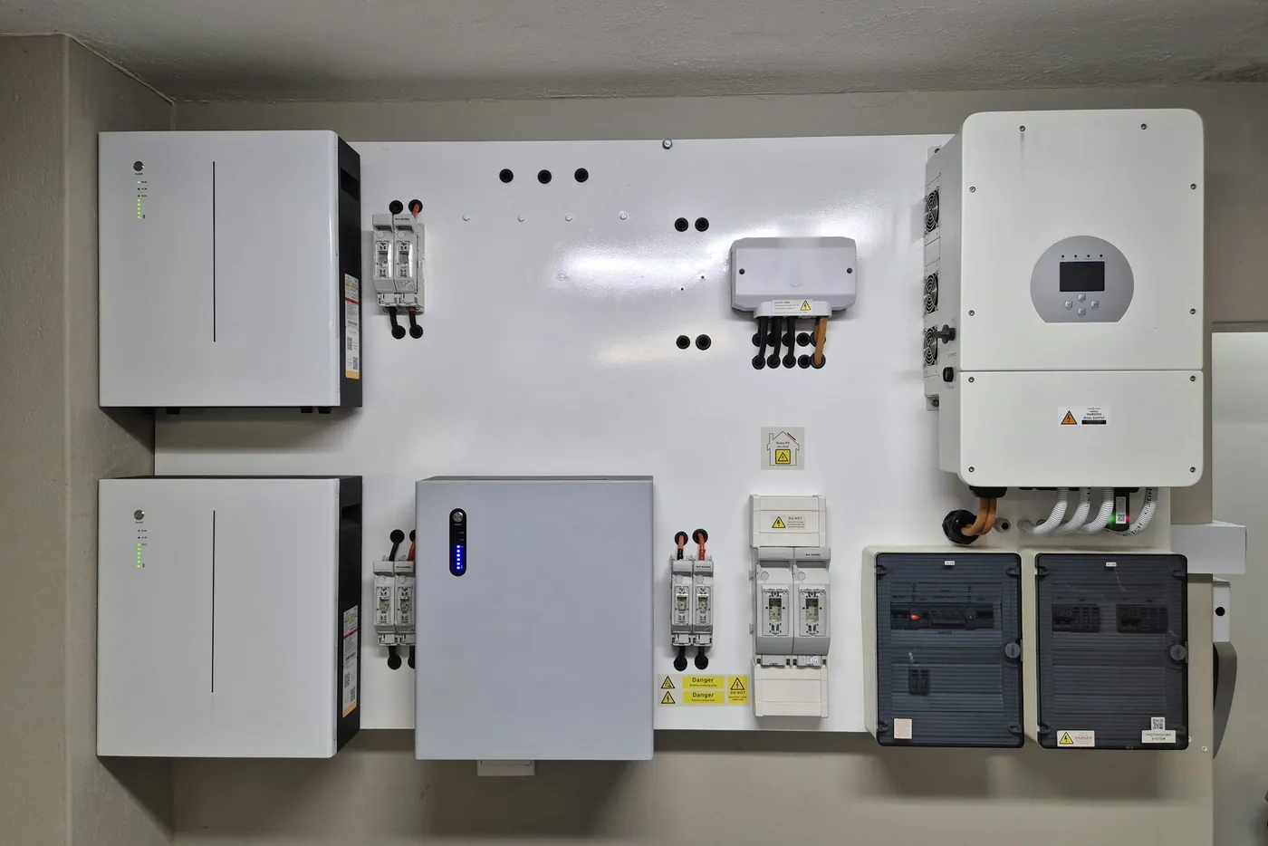 Drei Batteriemodule, ein Hybrid-Wechselrichter und Schutzschalter an einer weißen Montagewand im Technikraum (Böhlen, Landkreis Leipzig)