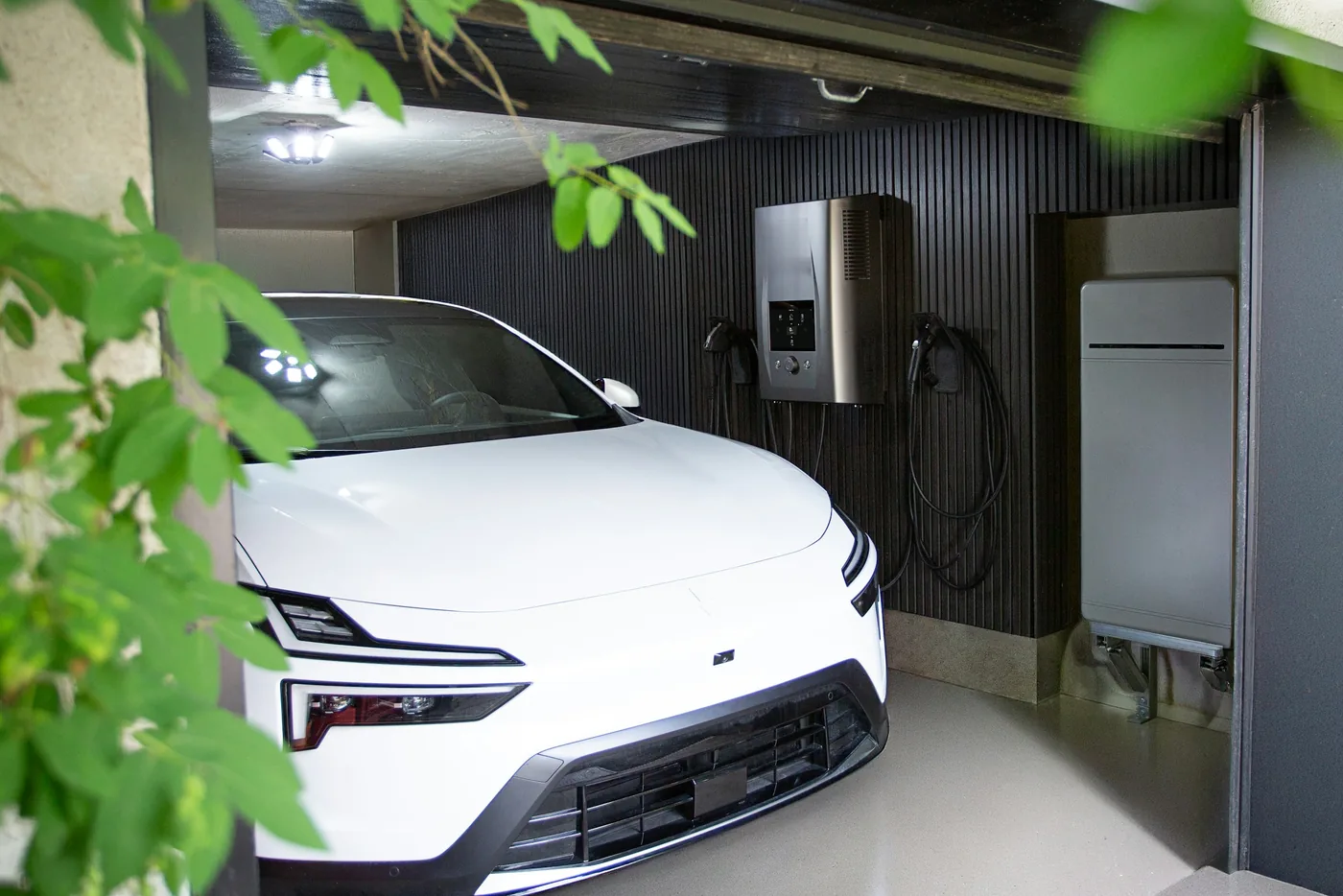 Garage mit Elektroauto, Wandladestation und bodenstehendem Batteriespeicher an einer dunklen Holzwand (Obersontheim, Landkreis Schwäbisch Hall)
