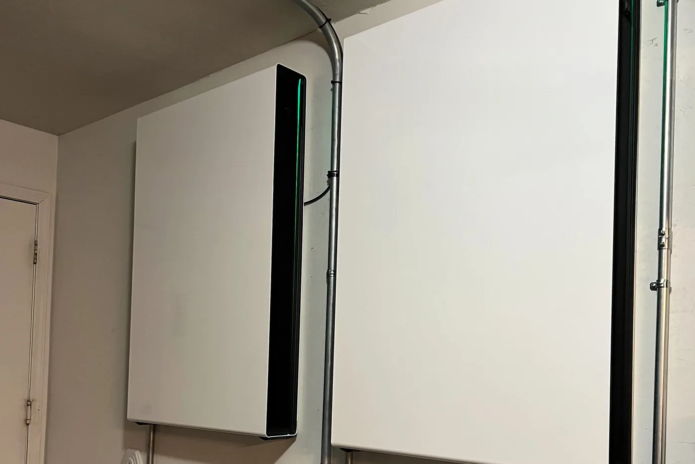 Zwei weiße Batteriespeicher an der Wand eines Technikraums, verbunden durch Leerrohre (Billwerder, Hamburg)