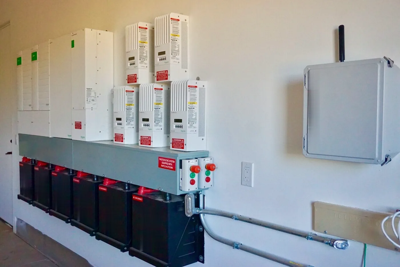 Laderegler und Wechselrichter über einer Reihe schwarzer Batteriemodule an einer hellen Wand (Tremsbüttel, Kreis Stormarn)