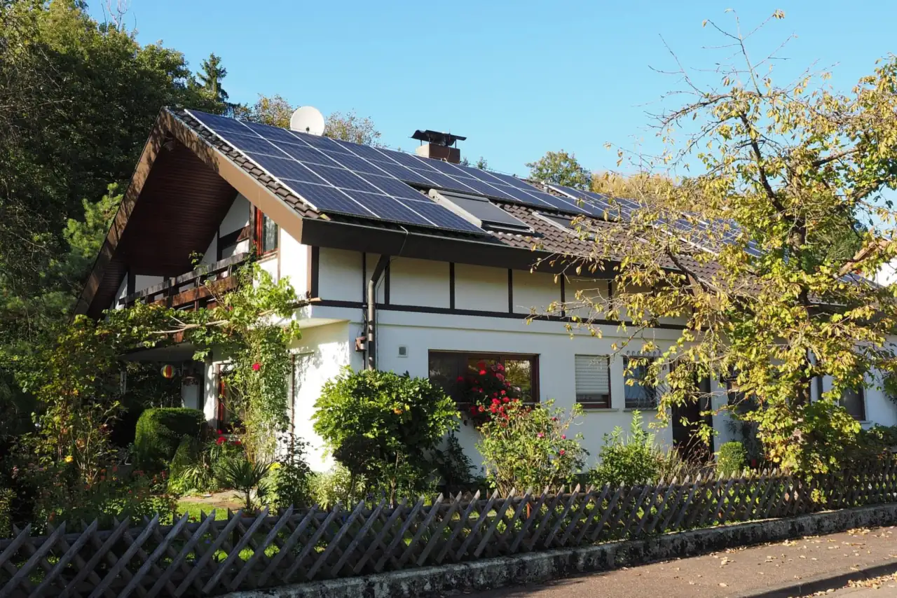 Einfamilienhaus mit Solaranlage auf dem Dach, Vorgarten und Holzzaun an einem sonnigen Tag (Berkenthin, Kreis Herzogtum Lauenburg)