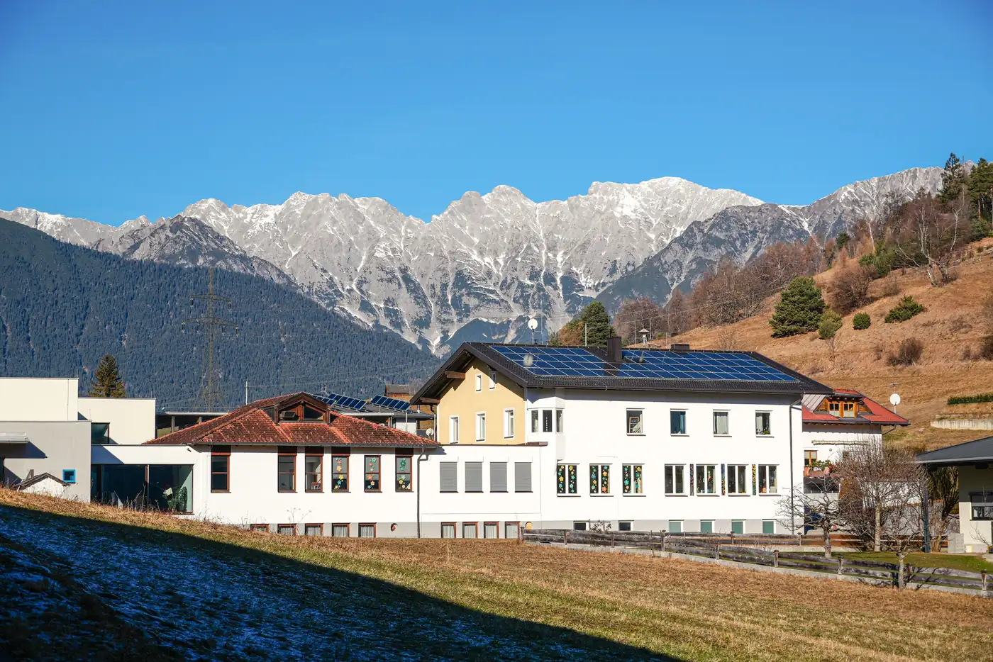 Weiße Häuser mit Photovoltaik auf den Dächern vor einer verschneiten Bergkette in Tirol (Dreetz, Landkreis Ostprignitz-Ruppin)