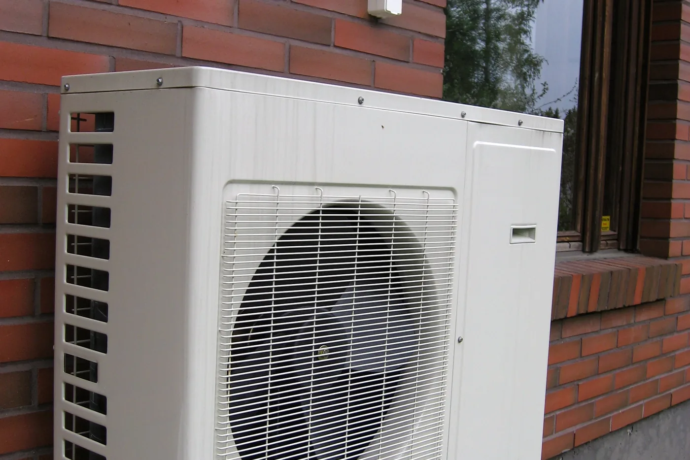 Außeneinheit einer Wärmepumpe an einer Backsteinwand neben einem Fenster